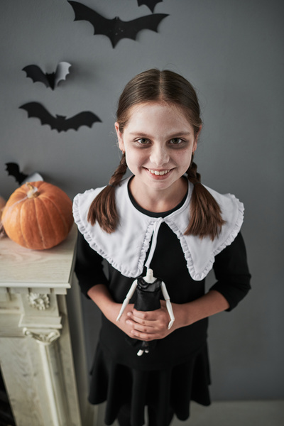 Girl in Halloween Costume Holds Doll without Head on Background of Bats